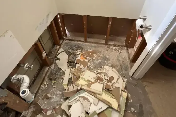 Bathroom walls stripped around a tub with debris on the floor