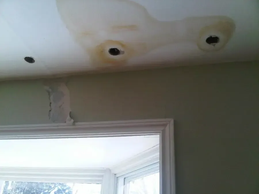 Ceiling stains and damaged areas above a window